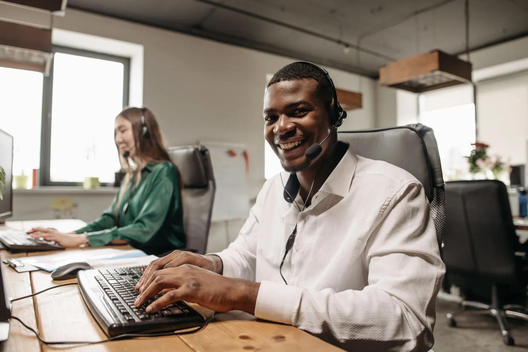 Smiling contact centre agent wearing a headset, typing at his desk