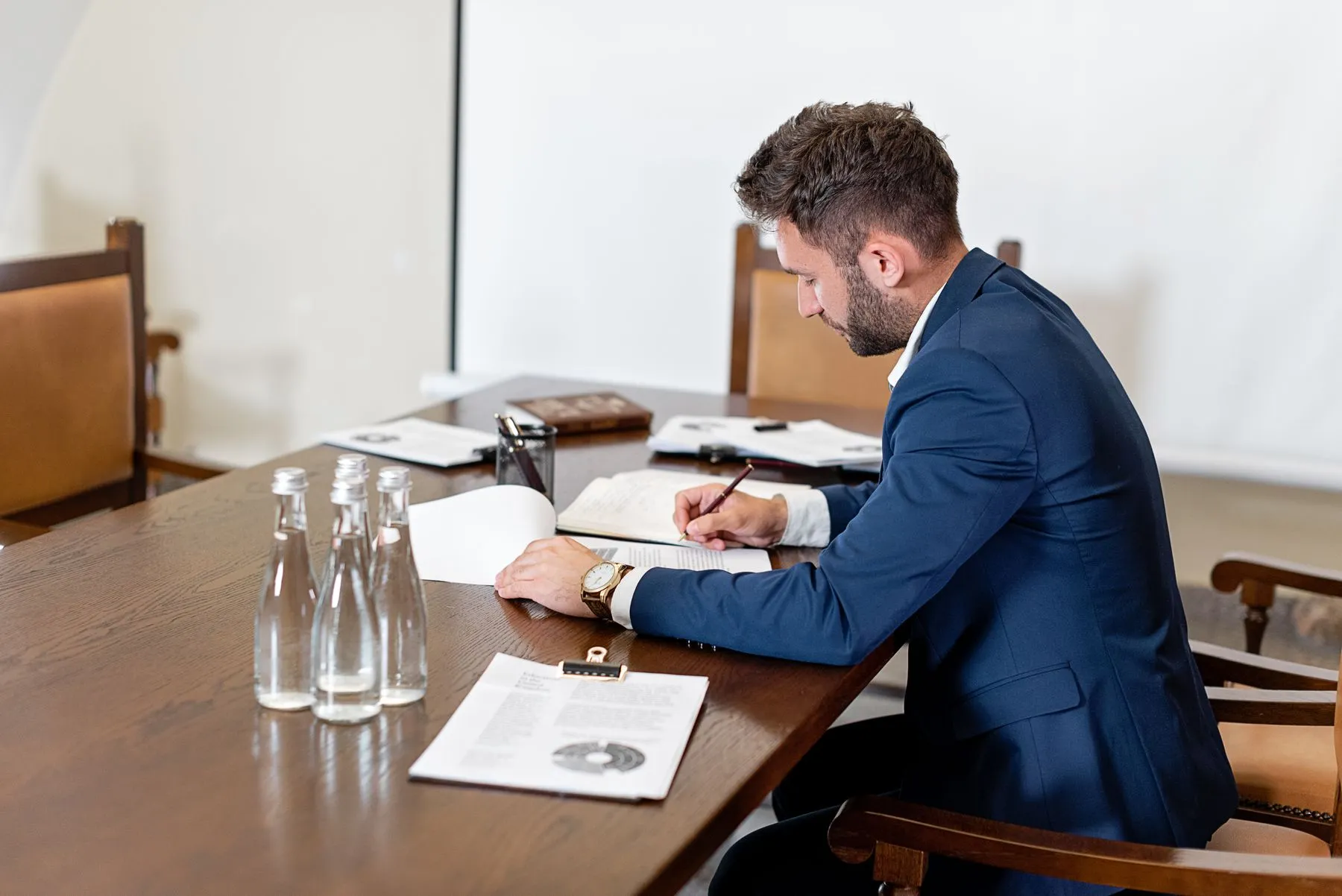 Man in a suit reading documents at a boardroom table