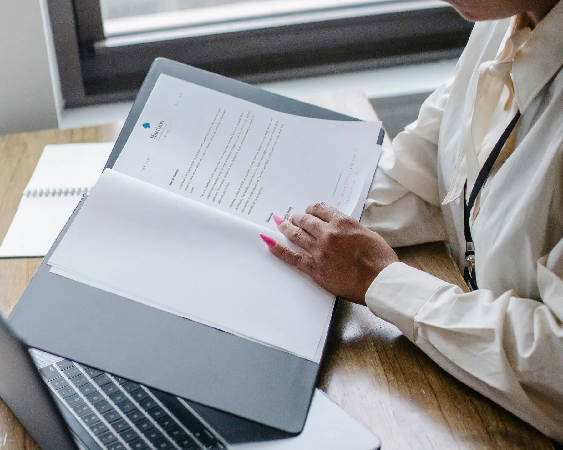 Woman reviewing paperwork at a desk beside a laptop